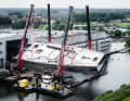 Four mobile cranes arrived to turn the aluminium hull, two of which were parked on pontoons