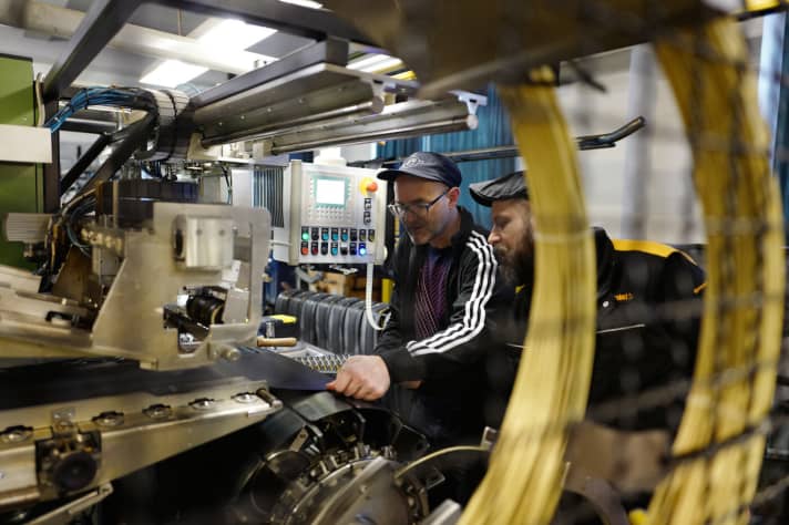   At last! Mission for colleague Lesewitz. The tyres are glued together on a complicated-looking machine. One turn of the roller and the carcass is ready. Another turn and the tread is on. Now the labels and the aramid threads on the sides. The raw tyre is finished. Well, a few intermediate steps are still necessary. Tyre builder Steffen Krüger patiently lends Lesewitz a hand and reveals a few secret tricks in the slang of his native Brandenburg. For example, the trick of how to properly tear the rubber from the roll. "Here, put your foot on the switch - then just pull the end off in one go and pull it straight off."