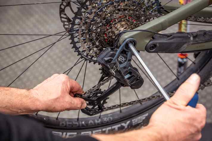 Pull the rear derailleur backwards by the cage until the chain is tensioned. The screw on the rear derailleur is tightened in this position.