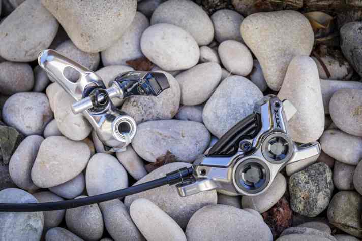 Welche dieser Shimano Bremsen hat wohl mehr Bremspower? Die Felgenbremse von 1982 ist es sicher nicht. Die neue XTR Vierkolben-Scheibenbremse ist dagegen ein richtiger Anker.