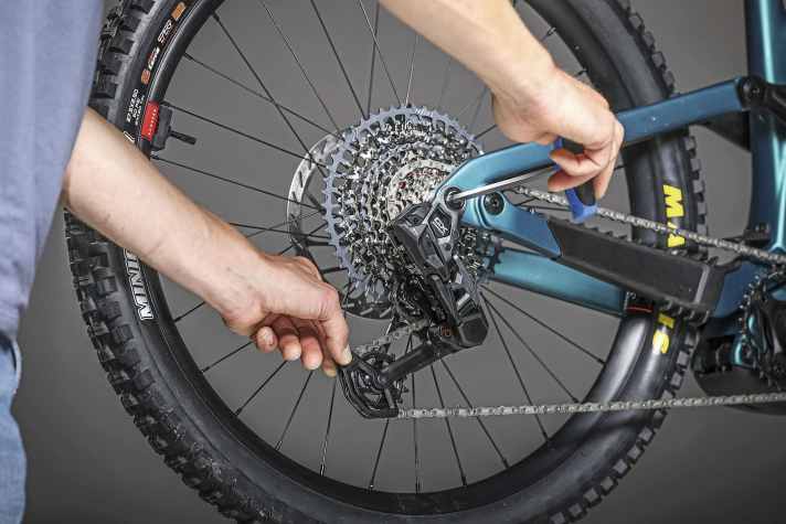 Mit der einen Hand das Schaltwerk am Käfig nach hinten ziehen, bis die Kette gespannt ist. Mit der anderen Hand die Hauptbefestigungsschraube des Schaltwerks anziehen.