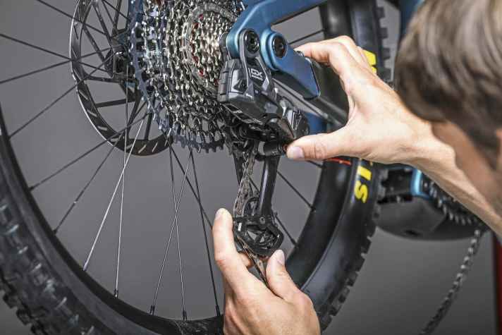 Mit dem roten Knopf wird der Schaltkäfig in der Setup-Position arretiert. Achtung: Den Käfig am langen Arm zum unteren Röllchen einrasten, NICHT ganz vordrücken und über dem oberen Röllchen fixieren.