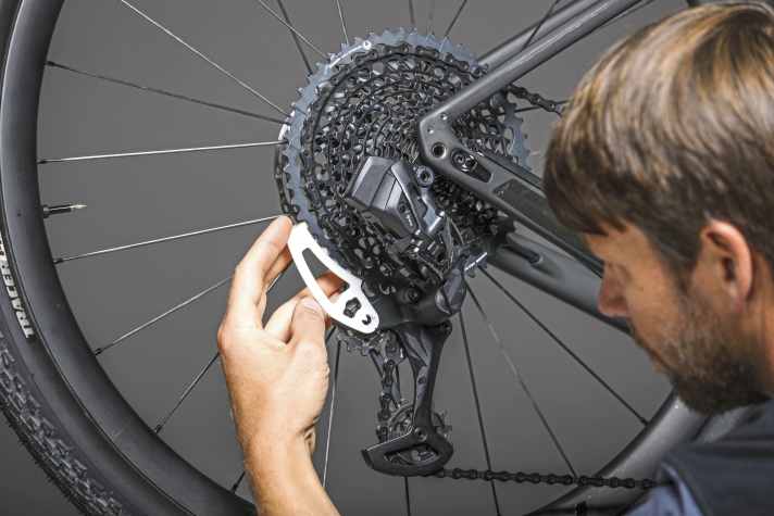 Mit der Kette auf dem zweitgrößten Ritzel wird das Tool auf das größte Ritzel gesteckt und Richtung Schaltkäfig geschoben. Der Pfeil soll dann direkt auf der Befestigungsschraube des oberen Schaltröllchens landen.