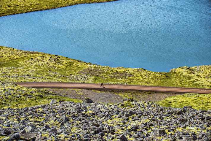 Iceland like in a picture book: moss-covered hills, red gravel tracks, blue lakes.