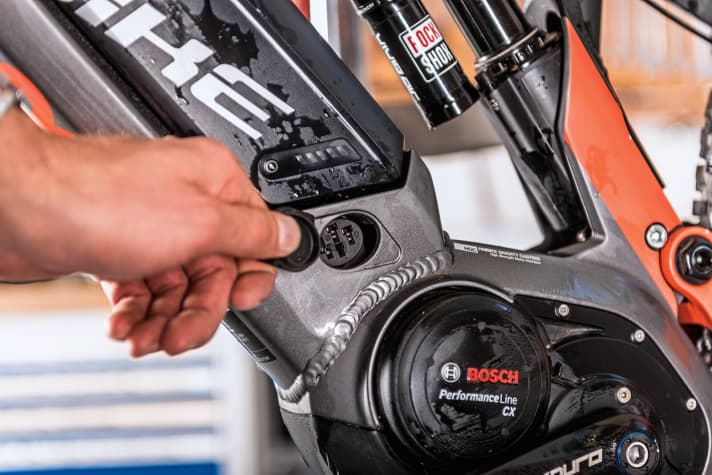    4 Lade-Port: Bei allen E-MTBs sind die On-Board-Lade-Ports der Akkus mit Abdeckungen versehen. Bei der Reinigung des Bikes sollten Sie darauf achten, dass die Abdeckungen geschlossen sind. Kommt doch einmal Wasser dran und schlimmstenfalls auf die Kontakte, entnehmen Sie den Akku, tupfen Sie die Feuchtigkeit ab und lassen das Bike in der Sonne trocknen. Grundsätzlich sind die Bikes spritzwasserfest gedichtet. Wenn der Lade- Port zu ist, kann also auch beim Durchfahren einer Pfütze oder bei einem Regenguss nichts passieren. Es empfiehlt sich allerdings, die Kontakte einmal im Jahr mit Kontaktfett (im Elektronik-Zubehörhandel erhältlich) zu pflegen.    