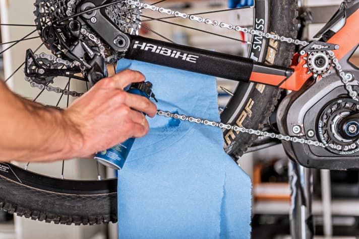    7 Lubricate the chain: You must lubricate the chain after cleaning. Use the cloth to prevent chain oil from getting onto the brake disc when spraying. Spray the chain oil onto the inside of the chain while turning the crank so that the oil is distributed over the entire length of the chain. Once you have applied the chain oil, turn the crank and shift through all gears several times. Then wipe the excess chain oil off the chain with the cloth. Ideally, you should lubricate the chain of an e-MTB before every ride. The drive is subjected to enormous strain on e-mountainbikes and regular lubrication reduces wear a little.