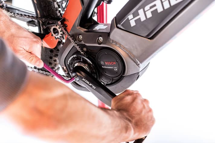    1 Kurbel abnehmen: Wann nimmt man das Ritzel vorne ab? Um nach einer Saison den Zustand des Ritzels zu checken, oder um die Übersetzung des E-MTB zu verbessern. Wer in den Bergen viele, steile Anstiege fährt, greift vorne gerne zu kleineren Zubehörritzeln. Achtung: Erst mit der 2017er-Bosch-Software ist ein Ritzeltausch ohne Neuprogrammierung der Übersetzung beim Fachhändler möglich. Wer sich nicht sicher ist, lässt sich das Update beim Händler aufspielen. Um die Kurbel abzunehmen, mit dem Inbus die Kurbelschraube gegen den Uhrzeigersinn öffnen. Im Bild ist ein Abzieher in der Kurbel integriert, für Kurbeln ohne benötigt man einen separaten Kurbelabzieher.
