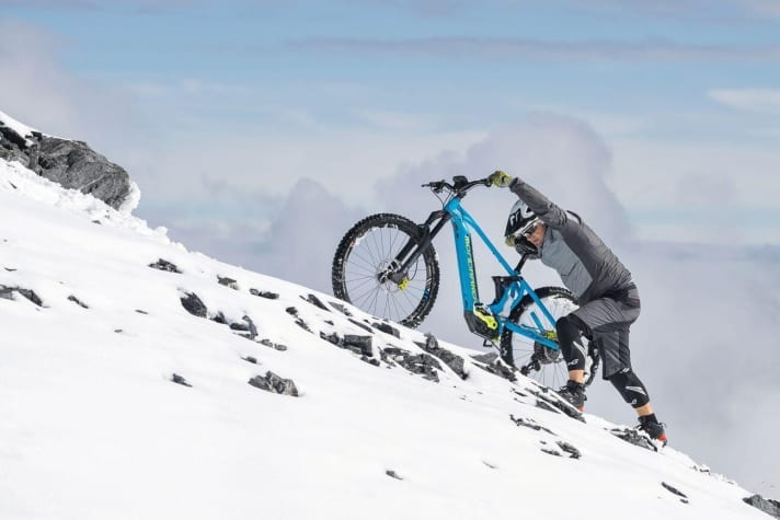   USING THE PUSH ASSIST EFFICIENTLY - The assistance opens up new terrain, especially in winter. Steep climbs that are simply not possible with a classic bike can be easily mastered with an E-MTB. But at some point, physics shows us the limits here too. When the rear wheel spins, the only thing that helps is pushing. The new, effective pushing aids take the fear out of steep climbs in the snow. If you know how to use them effectively, you can even make more energy-saving progress than on foot. The trick here is also to put as much pressure as possible on the rear wheel. First lower the saddle. Now press your upper body onto the saddle. This will put pressure on the rear wheel. Depending on the steepness of the gradient, you can now adjust the pushing speed using the gears and fine-tune it with the rear brake.