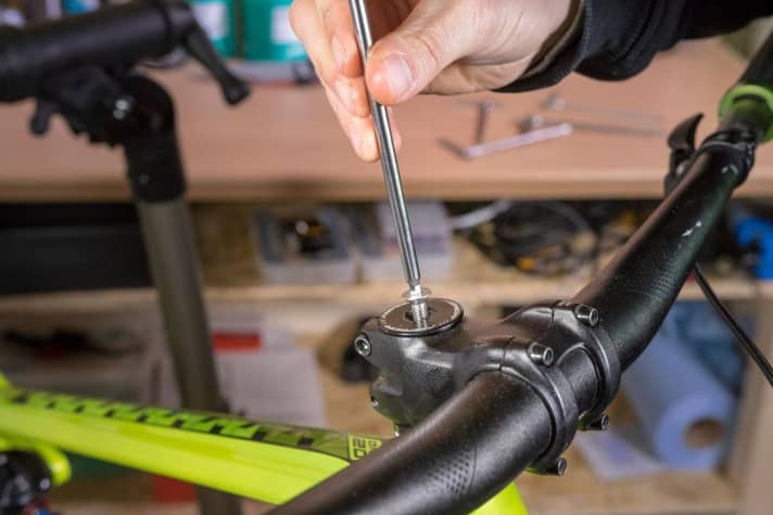 To prepare, remove the front wheel and dismantle the front brake. Then loosen the two stem bolts that clamp the stem to the steerer tube. One turn of each screw is often sufficient. Then unscrew the Ahead cap (picture) and put it to one side. Caution: When unscrewing the Ahead cap, hold the fork with one hand, otherwise it will slip out of the head tube.