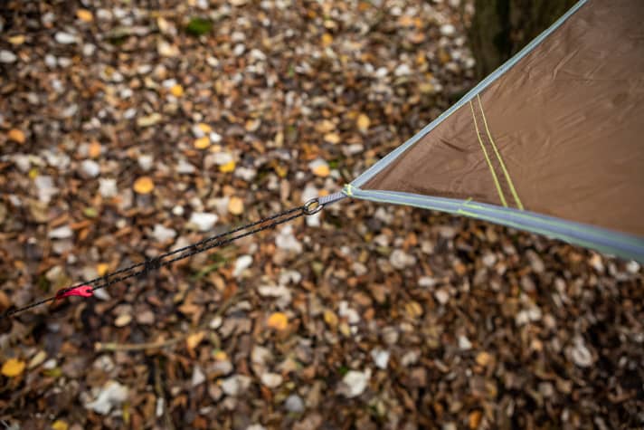 Lightweight aluminium pegs are also included. The tensioning cords remain on the tarp and wait in the corner pocket for use. The workmanship is very good. The all-round hem dissipates the tensile forces. The red aluminium adjusters are robust and provide a colourful counterpoint.