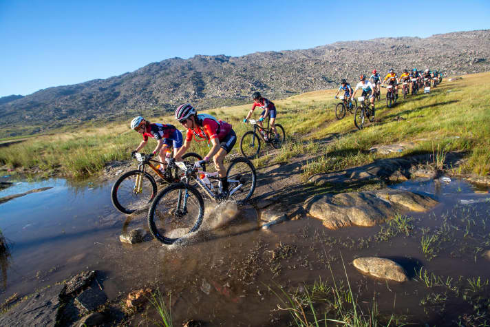   Die dreifache Cape Epic-Siegerin Ariane Lüthi führt das Damenfeld im ersten Teil der Etappe durch ein Bachbett.
