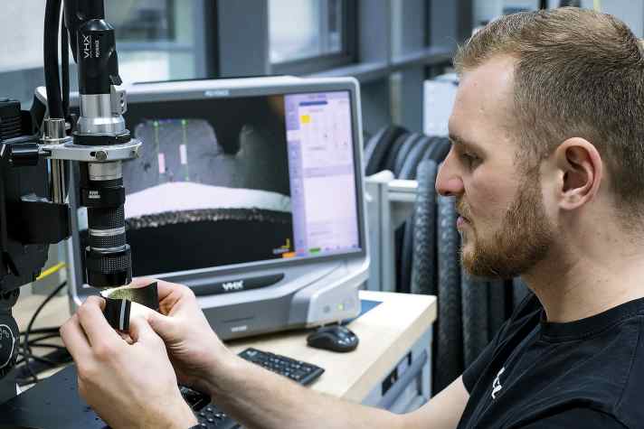 Lars Funke, Labormitarbeiter, mikroskopiert Reifenquerschnitt mit Schutzlage im Compound.
