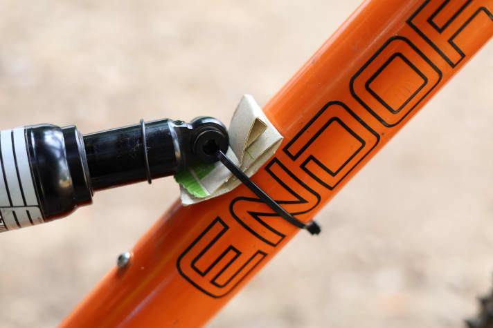 Da sich der Dämpfer nicht mehr ausbauen lässt, muss er anderweitig fixiert werden, ohne die maximale Kompression des Hinterbaus zu blockieren. Ein Kabelbinder und ein Stück Pappe halten ihn an Ort und Stelle, ohne dass der Rahmen weiter beschädigt wird.