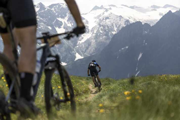 Maxxis BIKE Transalp 2024: the single trail through the flower meadow in front, the view of the glaciers behind.