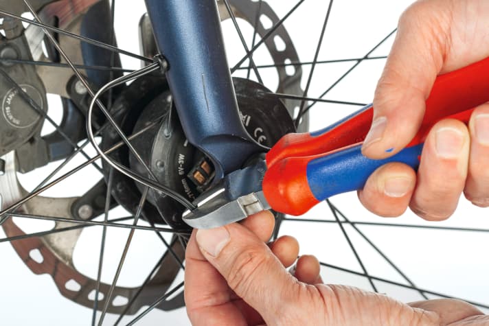 Ziehen Sie das Dynamokabel am Austritt aus der Gabel mit etwas Spiel am Gabelkopf handfest. Lassen Sie gut 4 Zentimeter Überstand nahe der Radachse, kürzen Sie das Kabel und isolieren Sie 1,5 Zentimeter ab.