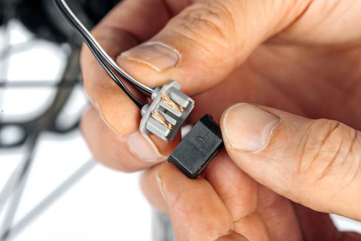 Schieben Sie die blanken Enden in den Stecker und fügen Sie beide Hälften zusammen. Verbinden Sie Kabel und Nabendynamo.