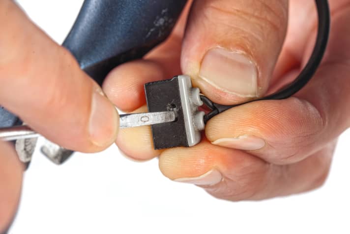 Ziehen Sie dann den Stecker vom Nabendynamo und entnehmen Sie das Vorderrad. Öffnen Sie das Stecker-Gehäuse mit einem kleinen Schraubendreher. Die Kabelenden lassen sich bei auseinandergenommenen Hälften leicht aus der Passung ziehen.