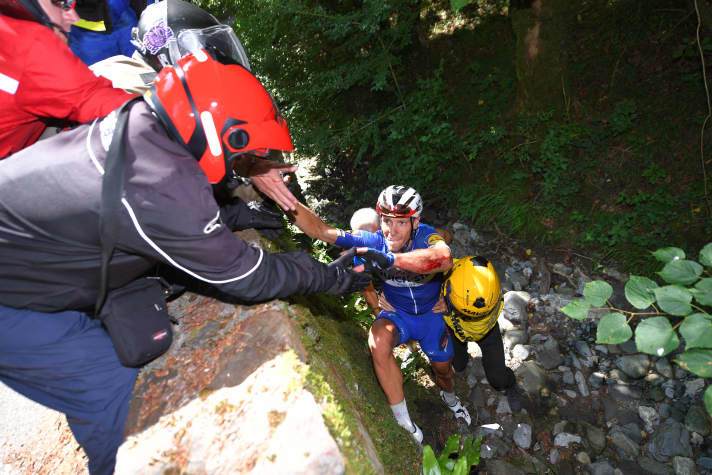 Tour de France 2018 : Philippe Gilbert passe par-dessus un mur d'enceinte. Plusieurs assistants le hissent ensuite en haut du talus.