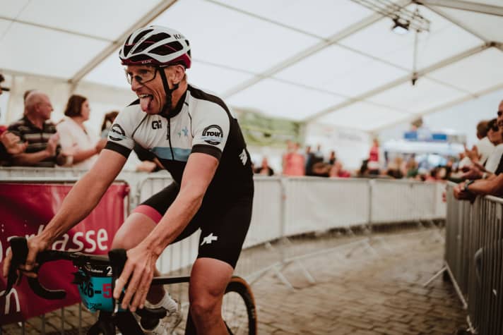 Geschafft! Schlussfahrer Martin fliegt kurz vor 14 Uhr ins Ziel. Das ganze Bierzelt feiert ihn und die anderen Fahrer mit Applaus, die Zuschauer und Teamfahrer stehen dicht gedrängt.