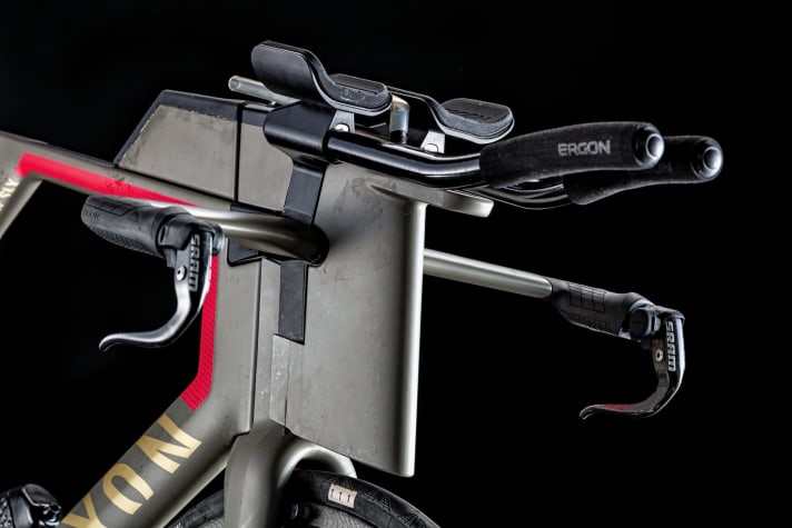   Cockpit sur mesure : pour réduire au maximum la surface frontale du vélo de Frodeno, Canyon a fraisé une pièce spéciale qui se trouve au milieu de la potence. Normalement, les accoudoirs du Speedmax CF SLX reposent plus à l'extérieur sur le guidon de base. Le réservoir d'eau, normalement adapté au guidon de série, a donc dû être fabriqué sur mesure. La boîte sur le tube supérieur, qui accueille les barres et les gels, est toutefois de série. Les accoudoirs sont en mousse spéciale très chère, issue de la technique médicale ; le modèle de série en est également équipé.