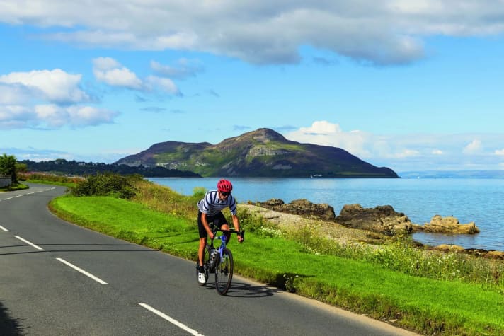 Kurvig: Die Küstenstraße mit dem vorgelagerten Felsen von Holy Isle im Firth of Clyde