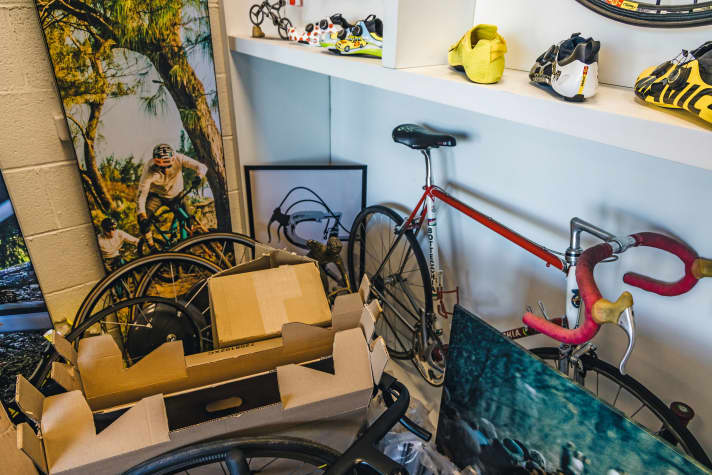 Un vélo de course de l'époque de Greg LeMond, protégé par des cartons contenant des prototypes, des objets de dévotion et des panneaux publicitaires.