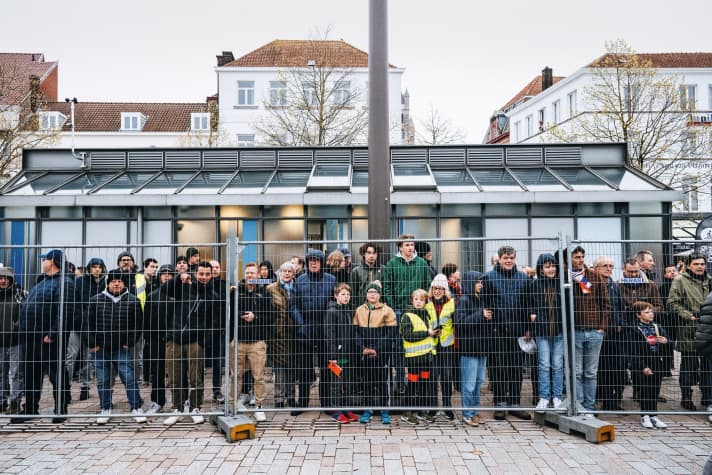 In the cold of the morning, fans wait behind the fence in Bruges to watch the professionals before the start