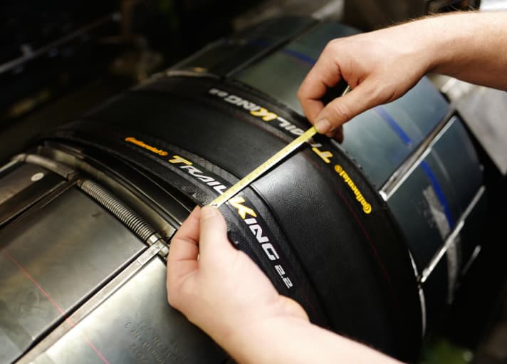   If you look over Steffen Krüger's shoulder for a while, you will be fascinated by the speed and precision of the work. Fine red laser beams (shown in the picture to the right of the tread) mark where the tyre needs to be fitted with tenths of a millimetre precision. When the tyre blank is ready, Krüger checks everything with the measuring tape. Phew! The Trail King 27.5 x 2.2 tyre from reporter Lesewitz passes the quality control.