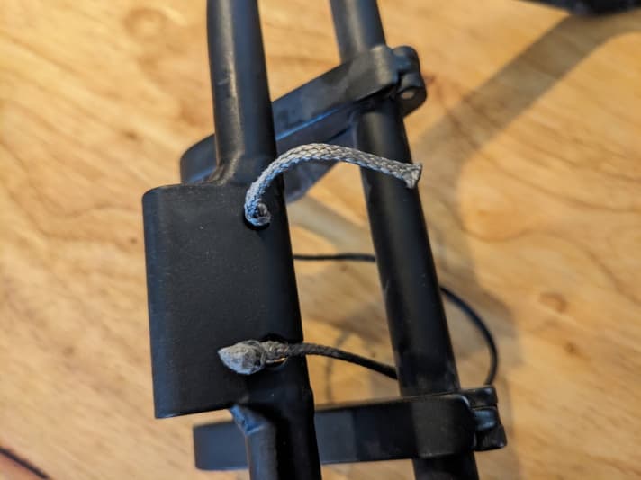 Montage des Stabilisierungsseils. Die Montage erfolgt am Rad. Als erstes wird ein Knoten an ein Seilende gemacht (oben im Bild), dann wird das Front-Rack richtig ausgerichtet. Ein  zweiter Knoten wird gemacht und das Seil in die dafür vorgesehene Öffnung eingeführt (im Bild unten). Im Test war es nicht leicht, die korrekte Position für Knoten 2 zu finden und wir brauchten etwa 10 Versuche bis es passte.