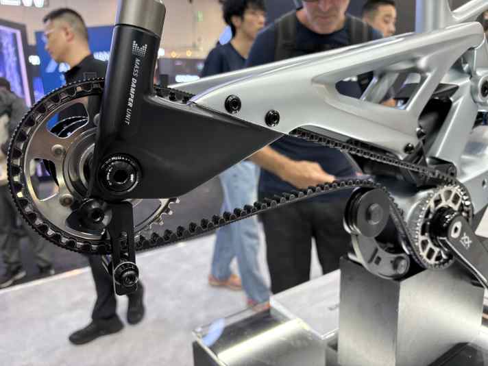 Power is transmitted via a chain or a belt. The belt tensioner looks quite substantial.