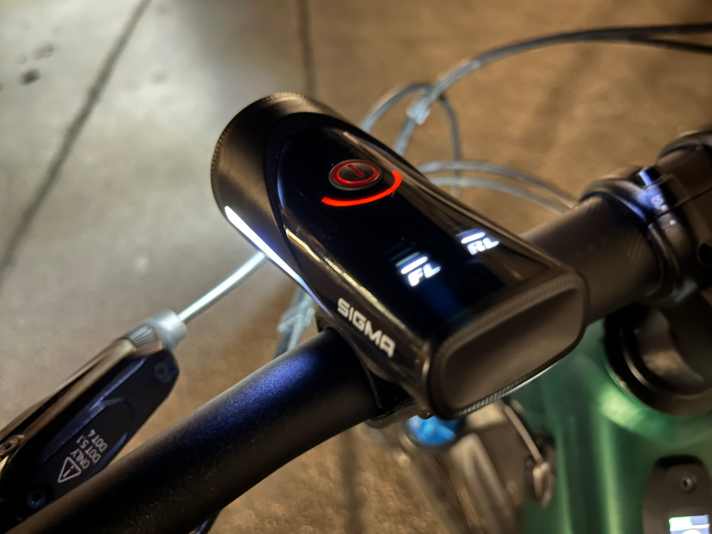 So funktionierts: Kurzes “Drück, Drück” und die Lampe und das Rücklicht gehen an. Mit weiteren kurzen “Drücken” verstellt man die Modi und somit die Lumen. Lang Drücken und die Lampe samt Rücklicht gehen aus. Hier gut zu erkennen: Die Akku-Anzeige für Lampe und Rücklicht (FL/RL).