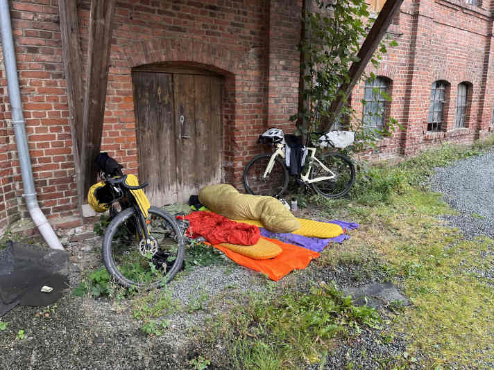 Gut gedacht, schlecht gemacht: Zwar gibts hier ein Dach, doch es ist zu hoch und zu klein. So wird der Regen vom Wind unters Dach getragen. Zudem ist eine Straße in Sichtweite mit möglichen Passanten, die sich für die schlafenden Bikepacker interessieren.