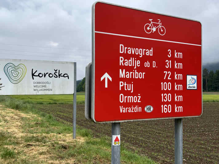 Willkommen in Slowenien. Grenzkontrollen gibt es seit dem EU-Beitritt nicht mehr. Eine große Tafel weist den weiteren Verlauf des Drauradwegs.