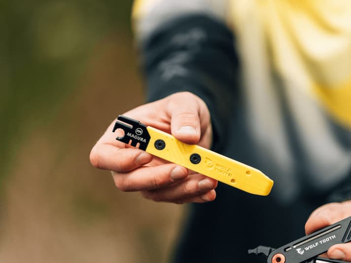 The brake-specific attachment has a brake disc alignment tool, a slotted 8 mm hole spanner and two measuring tools for checking the brake pad and disc. The yellow plastic part serves as a tyre lever.