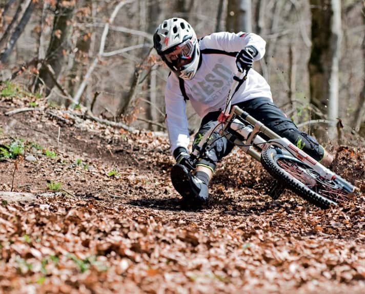   Apply the brakes and then lean in until the grip almost scrapes the ground. Because DH handlebars nowadays tend to be as wide as Arnie's shoulder section, the near-ground contact works even on smaller berms: FREERIDE tester Christian Schleker in a cornering frenzy.