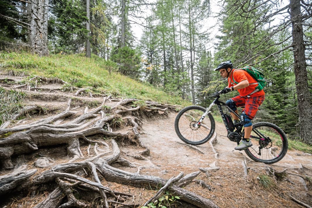 Like taking the lift to the top: The principles of pedal management, which have already been mentioned many times, come into play again on the steep uphill obstacle. Just as with the obstacle on easy terrain, the pedal sequence must be adapted and optimised for the terrain. The trick with high obstacles is to deal with the additional power of the motor, as the movement sequence begins in a standing position. You have to look at how to dose the motor power to prevent the rear wheel from spinning. Choosing the right level of assistance is very important here.
 Turbo mode is ideal for very good grip. However, when things get slippery, it quickly reaches its untameable limits and you have to switch to Sport mode or Tour mode. The actual movement sequence begins one wheel length before the obstacle in a gear where you cover about one wheel length with half a turn of the pedals. In terms of body position, you tend to be further forwards with this technique and therefore have less pressure on the rear wheel to get traction on the ground (photos 1 and 2) ...