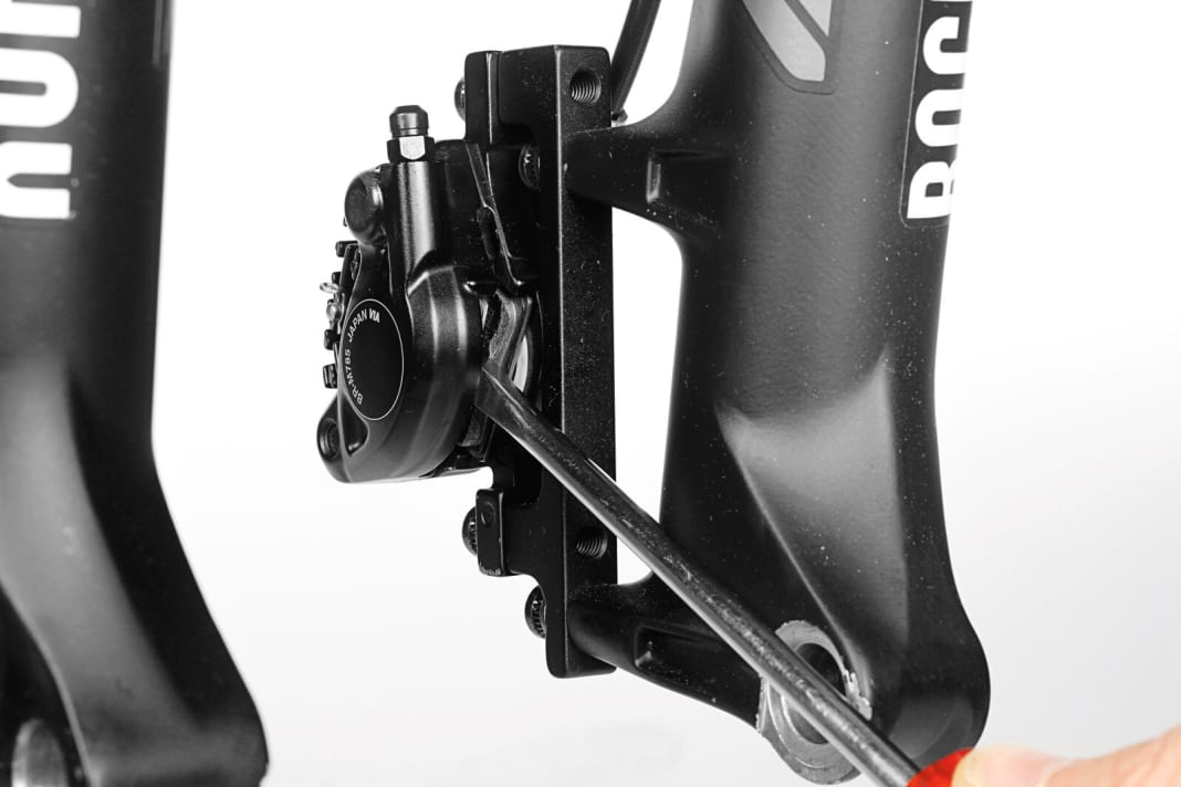 1. Kolben zurückdrücken: Bevor Sie die Beläge ausbauen, drücken Sie mit einem flachen Werkzeug die Bremskolben zurück in die Ausgangsstellung im Bremssattel. Bei ausgebauten Belägen können die Kolben leicht beschädigt werden. Nutzen Sie also lieber die verschlissenen Beläge als Schutz. 