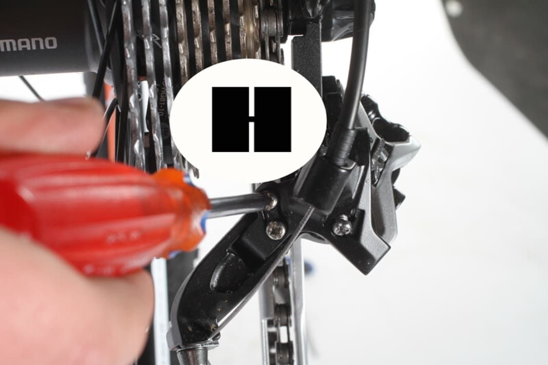 1. bring the chain onto the largest chainring. Adjust the right stop of the rear derailleur so that the upper derailleur pulley is positioned slightly to the right under the smallest sprocket. To do this, turn screw H to the left to move the stop further outwards and to the right to move it inwards.