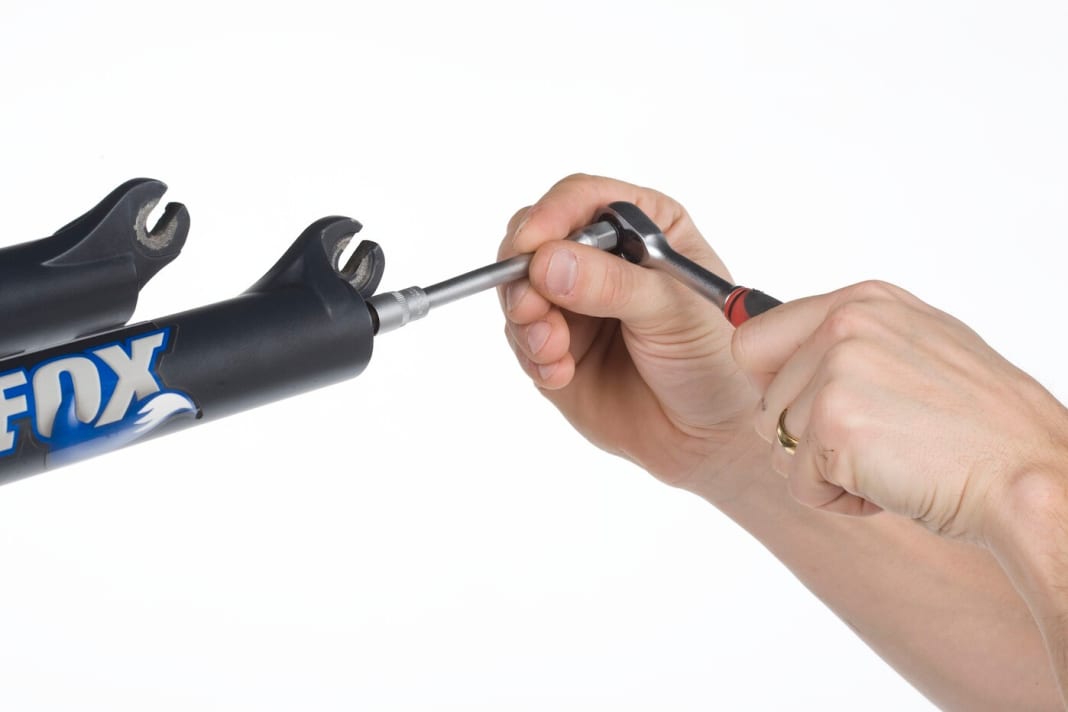 Tauchrohre lösen: Öffnen Sie mit einem 10-Millimeter-Steckschlüssel die beiden Muttern auf der Unterseite der Gabelholme. Bei RLC-Modellen müssen Sie auf der Dämpfungsseite vorher das blaue Einstellrad für die Auslösehärte des Lockouts entfernen (2 mm Inbus-Schraube). Drehen Sie die Muttern so weit heraus, dass noch etwa drei Gewindegänge greifen.