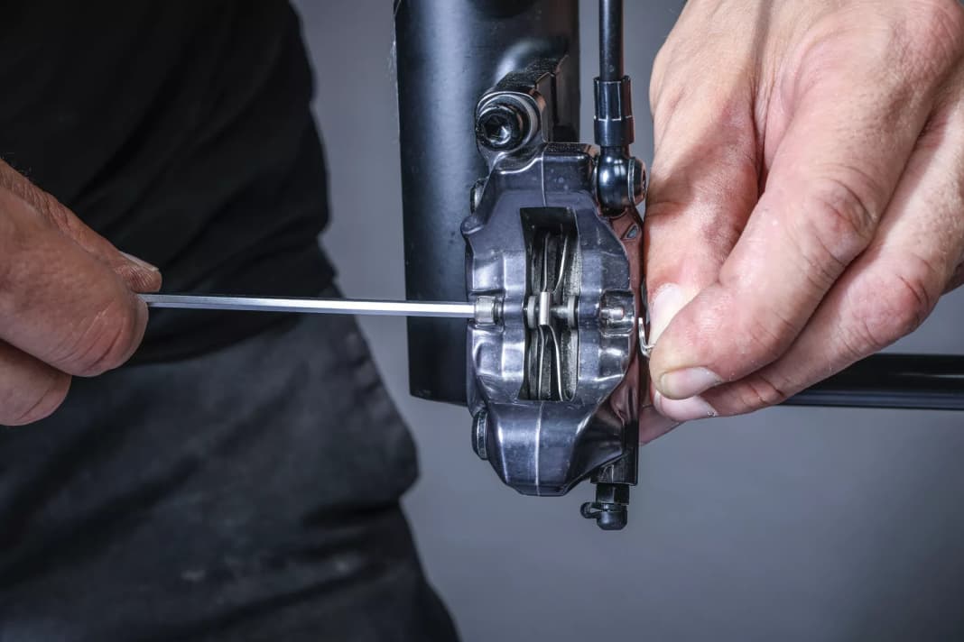 1 Remove the locking screw: Before you start replacing the brake pads, use a flat tool to push the brake pistons back as far as possible between the old brake pads. This will create space for the new, thicker pads. Now remove the retaining ring and then the retaining screw.