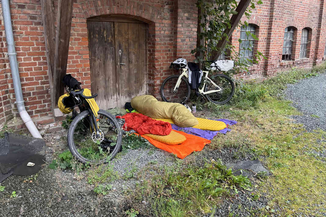 Gut gedacht, schlecht gemacht: Zwar gibts hier ein Dach, doch es ist zu hoch und zu klein. So wird der Regen vom Wind unters Dach getragen. Zudem ist eine Straße in Sichtweite mit möglichen Passanten, die sich für die schlafenden Bikepacker interessieren.