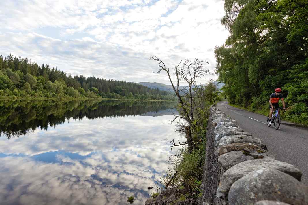 Spiegelbild: Eine verschlungene Straße führt durch den Märchenwald der Trossachs, inklusive See- und Himmelblick wie hier am Loch Achray.