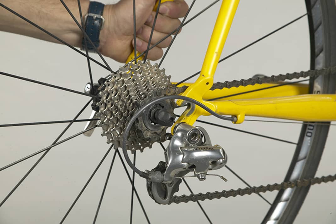 1. Bei nach hinten offenen Ausfallenden geht der Laufradwechsel am besten, wenn man das Rad in einen Montageständer hängt. Unterwegs ist es hilfreich, den Sattel des Rades an Zaun oder Mauer anzulehnen. Kette aufs kleinste Ritzel schalten, Bremse und Schnellspanner öffnen. Halten Sie den Hinterbau des Rahmens fest und ziehen Sie das Laufrad nach hinten aus den Ausfallenden heraus, um die Achse dann gleich nach vorne und unten hin am Schaltwerk vorbei zu führen.