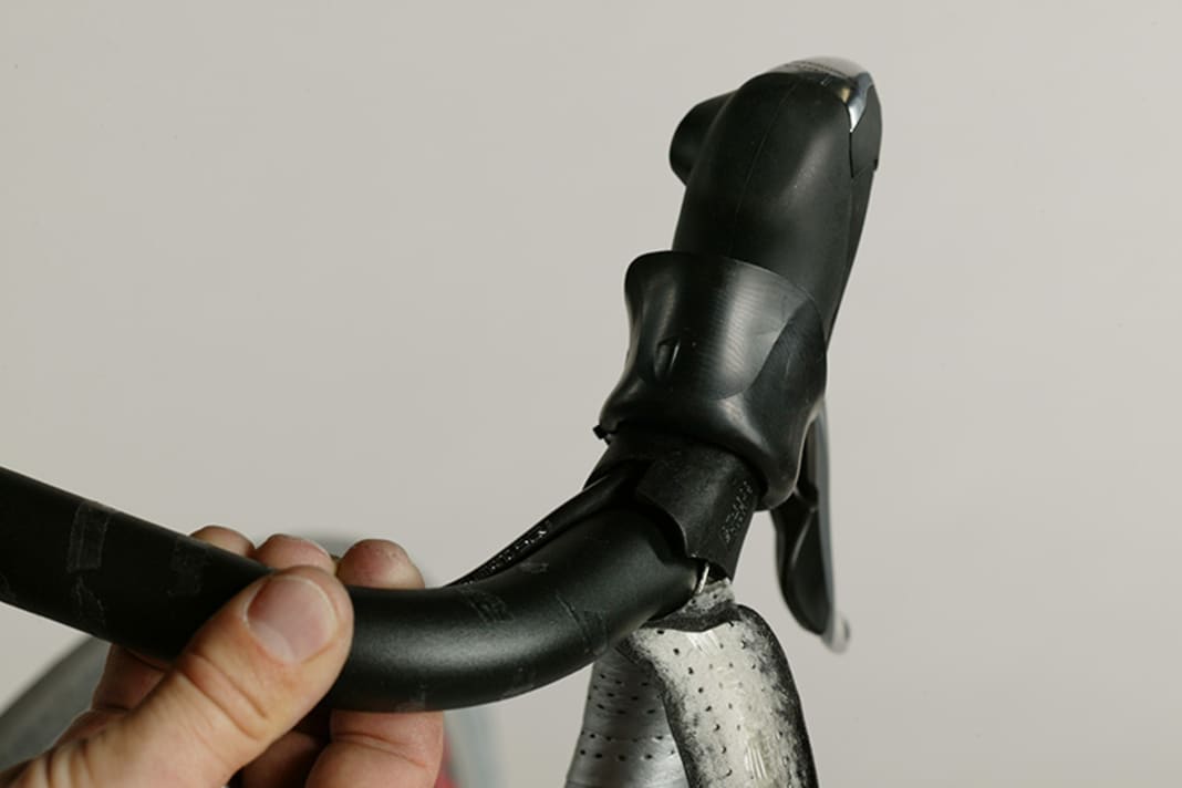 1. Klappen Sie den Griffgummi des Bremshebels nach vorne um und stecken Sie die Bremszugaußenhülle von der Lenkerseite her oben in den Bremsgriff, bis er innen ansteht. Prüfen Sie dies, indem Sie durch die Kontrollaussparung im Griff schauen. Legen Sie die Hülle in die Sicke entlang des Lenkers bis an die verdickte Stelle neben der Lenkermitte. Hier endet später das Lenkerband, und der Zug tritt ins Freie.