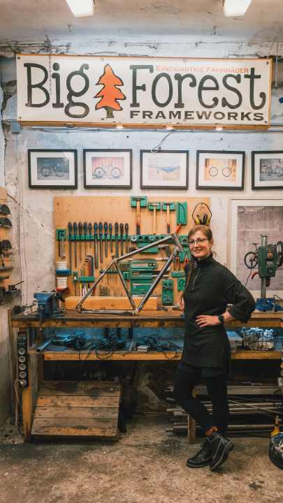 Eine stolze Juliane mit ihrem selbstgebauten Gravelbike-Stahlrahmen in der Werkstatt von Big Forest Frameworks.