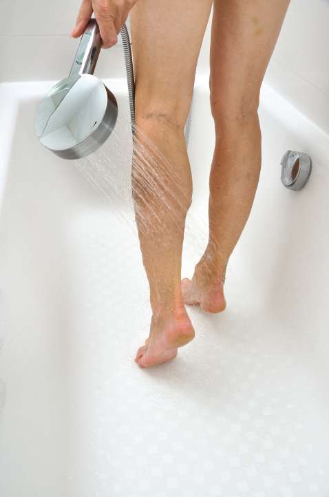Seniorin spült in der Badewanne ihre Beine ab