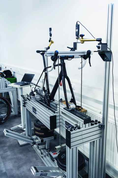 Machine à pression : un poids de 40 kilogrammes est introduit dans le guidon à hauteur des poignées de frein via une barre transversale, la fourche peut s'écarter via un galet. On mesure la déformation verticale de l'ensemble du système.