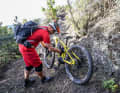 Damit das E-MTB bequemer auf dem Rücken sitzt, stellen Sie die Gurte des Rucksacks so eng ein, dass dieser möglichst nah an den Schultern sitzt. Die Kurbel mit Pedal zeigt nach unten. Greifen Sie jetzt das Bike am Gabelholm und irgendwo im Bereich der Mitte des Sitzrohrs (Bild 1).