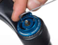 Remove the lockout button: On Fox RL and RLC suspension forks, open the lockout completely (position approx. 11 o'clock). Loosen the three 1.5 millimetre Allen screws only slightly (do not unscrew them completely) and carefully lift the blue lockout lever upwards. ATTENTION: There is a tiny ball in three holes on the underside of the lever. Do not lose them! Lift the adjustment wheel for the rebound (compression) upwards and out.