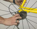 2. si vous n'y parvenez pas en un seul élan, posez la roue sur le sol et saisissez le dérailleur à l'avant du parallélogramme. Appuyez avec le pouce sur la cage de la poulie de guidage vers le bas. Le dérailleur ainsi tendu libère un espace par lequel la fusée d'essieu et l'écrou de serrage rapide peuvent se glisser si vous poussez un peu la roue par l'arrière, par exemple avec le genou.